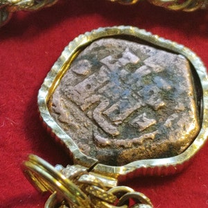 May include: A gold chain necklace with a round pendant featuring an antique coin with Arabic script. The coin is set in a gold frame.