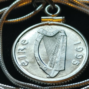 Puede incluir: Un collar de cadena de plata con un colgante que presenta una moneda irlandesa de plata con el arpa de Irlanda y el año 1966. La moneda está rodeada por un borde de plata.