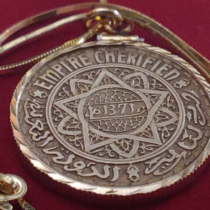 May include: A gold pendant necklace with a silver coin featuring the words "Empire Cherified" and the year "1871" in Arabic script. The coin is surrounded by a decorative border.