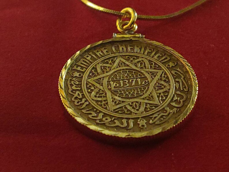 May include: A gold pendant necklace with a round, ornate pendant featuring a Star of David and the inscription "EMPIRE CHEMIFIED 1371".