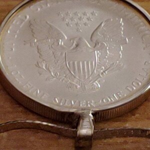 May include: A silver coin pendant featuring the American Eagle design. The coin is marked "ONE DOLLAR" and "1 OZ. FINE SILVER". The pendant is attached to a silver chain, showcasing a classic and valuable piece of jewelry.