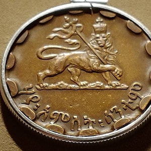 May include: A gold-colored coin with a lion holding a staff and a crown on its head. The coin has the text "ኢትዮጵያ" and "1940" around the edge.