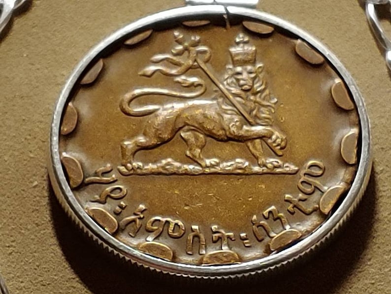 May include: A gold-colored coin with a lion holding a staff and a crown on its head. The coin has the text "ኢትዮጵያ" and "1940" around the edge.