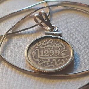 May include: A silver chain necklace with a silver pendant featuring an old coin with Arabic script and the date 1299.