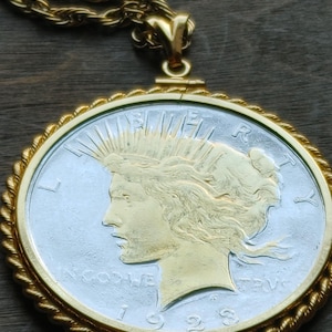 Pode incluir: Um colar de corrente de ouro com um pingente de prata e ouro Peace Dollar. O pingente apresenta um perfil de Liberty com a inscrição "LIBERTY" e "IN GOD WE TRUST". O ano "1928" está inscrito na parte inferior do pingente.