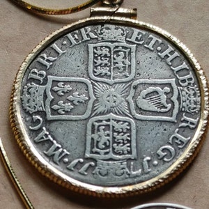 May include: A silver coin pendant with a gold-colored bezel and chain. The coin features a detailed design with text and heraldic symbols. The pendant is a vintage piece, suitable for collectors or as a unique accessory.