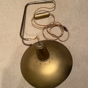 May include: A gold-toned metal ceiling light fixture with a round, flat shade and a curved arm. The light has a cord and plug.