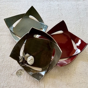Könnte beinhalten: Drei Keramik-Schalen in verschiedenen Farben: Grau, Braun und Rot. Die Schalen sind übereinander gestapelt und haben ein einzigartiges, geometrisches Design.