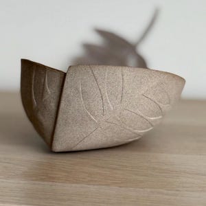 以下が含まれることがあります： 葉のデザインが施された薄い茶色のセラミックボウル。ボウルは角度が付いており、内側が見えます。
