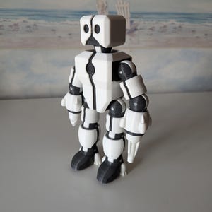 May include: A white and black articulated robot toy with a square head and two black eyes. The robot has posable arms and legs.