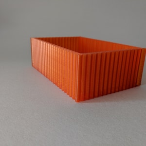 以下が含まれることがあります： オレンジ色の長方形の箱で、リブ状のテクスチャがあります。箱は空で、滑らかで光沢のある仕上げになっています。