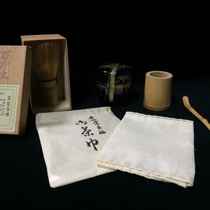 May include: A Japanese matcha tea set with a bamboo whisk in a box, a black tea bowl with bamboo design, a bamboo scoop, a bamboo holder, a white cloth, and a paper package with Japanese text.