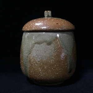 May include: A ceramic jar with a matching lid, featuring a speckled brown base and a light green glaze that drips down the sides. The surface has a visible crackle texture throughout the glaze, and the lid has a small, square-shaped handle.