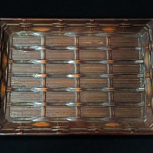 May include: A rectangular brown ceramic tray featuring a raised, molded basket-weave pattern across its surface. The design includes horizontal and vertical bands with small, orange-colored accents integrated into the border of the tray.