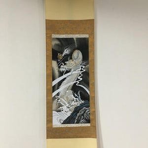 May include: A vertical hanging scroll featuring a detailed illustration of a white dragon rising from dark, turbulent waves. The dragon has long whiskers and scales, set against a black background with swirling white mist and a small golden orb.