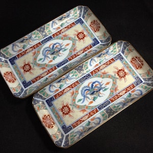 May include: Two rectangular ceramic trays with ornate designs. Each tray features a central oval with a blue bird, surrounded by red, blue, and gold accents. The borders have floral and geometric patterns.