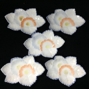 Könnte beinhalten: Ein Set aus fünf weißen Keramikschalen in Blattform mit gewelltem Rand. Jede Schale zeigt ein handgemaltes Design mit einem gelben Kreis in der Mitte, einem pfirsichfarbenen Halbkreis und einem hellblauen Farbverlauf sowie einem blauen Rand.