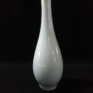 May include: A tall, slender ceramic vase with a smooth, pale celadon green glaze. The vessel features a bulbous base that tapers into a long, narrow neck, ending in a simple, circular opening. The surface has a glossy, reflective finish.