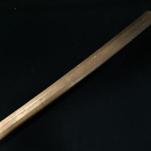 Könnte beinhalten: Ein langer, zylindrischer Holzstab mit einer glatten, hellbraunen Oberfläche. Das Objekt hat eine gerade, gleichmäßige Form mit leicht abgerundeten Enden und zeigt eine natürliche Holzmaserung über die gesamte Länge sowie eine solide Bauweise.