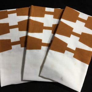 May include: Three folded white and brown patterned cloth napkins. The napkins have a white base with a repeating brown geometric design. The napkins are stacked on top of each other.