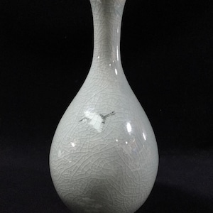 May include: A pale celadon-colored ceramic vase with a slender neck and rounded body. The vase features a crackle glaze and a painted crane design. The vase is a decorative item.