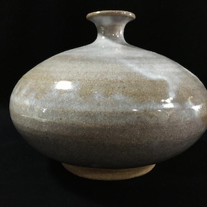 Könnte beinhalten: Eine Keramikvase mit einem breiten, abgerundeten Körper und einem schmalen Hals. Die Oberfläche weist eine gesprenkelte Glasur mit gemischten Tönen aus erdigem Braun, Grau und Weiß auf, die ein glattes, glänzendes Finish erzeugt.