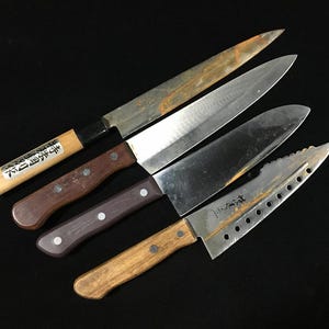 以下が含まれることがあります： 木製と複合材のハンドルが付いた、4つのさまざまなキッチンナイフ。 刃には摩耗や使用の兆候があり、錆も見られます。 ナイフは黒い背景に対して斜めに配置されています。