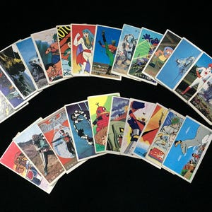 May include: A collection of vintage Japanese trading cards, featuring colorful illustrations of anime characters and scenes. The cards are arranged in a semi-circular pattern against a black background, showcasing a variety of designs and styles.