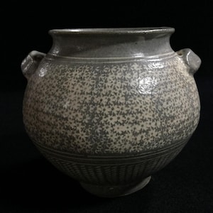 May include: A round ceramic jar with two small side handles, featuring a gray and white floral pattern on the upper body and a textured geometric cross-hatch design on the lower section, finished with a smooth, flared rim.