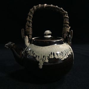 May include: A ceramic teapot with a dark brown base and a white, dripped glaze. It has a woven handle and a spout. The teapot is designed for brewing tea and has a lid with a small knob.