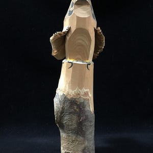 Könnte beinhalten: Eine handgeschnitzte Holzskulptur eines Falken. Der Falke sitzt auf einem Holzsockel, die Flügel leicht ausgebreitet. Die Skulptur ist mit natürlichen Farben bemalt, darunter Braun, Schwarz und Gelb. Die Augen des Falken sind detailliert, und die Federn sind präzise geschnitzt.