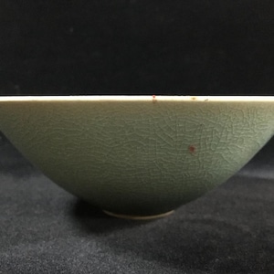 May include: A celadon ceramic bowl with a crackle glaze. The bowl has a wide, shallow shape with a slightly flared rim. The exterior has a textured surface with a network of fine cracks.