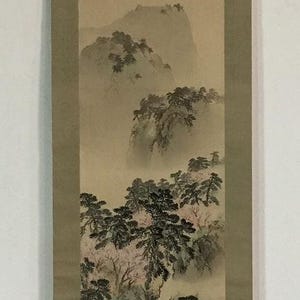 May include: A vertical hanging scroll featuring a landscape painting with ink and light watercolour washes. The artwork depicts misty mountains, dark green pine trees, and a small figure in a boat on a river, with a red seal mark in the corner.
