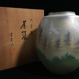 May include: A round, frosted glass vase featuring a painted scene of white cranes flying over a forest of green and gold trees. Beside the vase sits a square wooden storage box with black Japanese calligraphy characters and a red seal stamp.