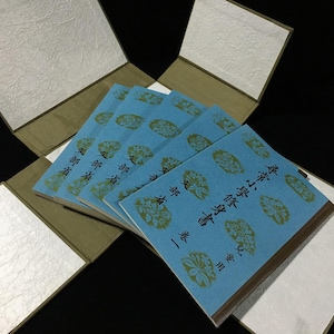 Könnte beinhalten: Ein Set aus fünf hellblauen Büchern mit goldenen Blumenmustern und schwarzem japanischen Text, die fächerförmig in einem beigefarbenen und weißen, strukturierten Klappetui angeordnet sind. Die Bücher tragen den Text 尋常小學修身書 卷一 und 文部省.