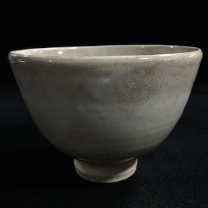 May include: A light beige ceramic bowl with a wide, rounded shape and a small, circular base. The bowl has a smooth, glossy finish with subtle variations in color, and a slightly textured surface.