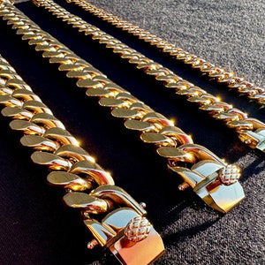 May include: Four gold chains of varying lengths and widths, all with a similar clasp design. The chains are laid out on a black surface.
