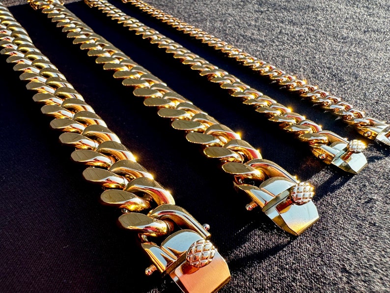May include: Four gold chains of varying lengths and widths, all with a similar clasp design. The chains are laid out on a black surface.