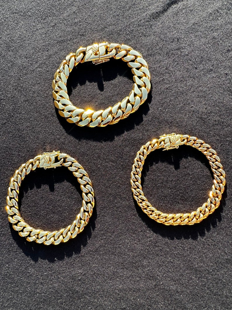May include: Three gold chain bracelets on a black background. The chains are all the same style, but different lengths.
