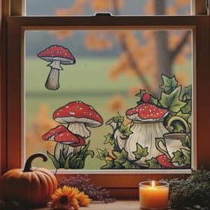 Op de afbeelding: Een raamscène met illustraties van paddenstoelen en een theepot. De paddenstoelen hebben rode doppen met witte stippen. Een pompoen, zonnebloem en brandende kaars staan op de vensterbank, wat een herfstthema creëert.