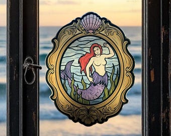 Puede incluir: Imagen decorativa enmarcada de una sirena con cabello rojo y cola morada. La sirena está en una escena marina con algas verdes y agua azul. El marco es dorado con una concha en la parte superior.
