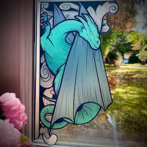 Puede incluir: Un drag&oacute;n azul verdoso con las alas extendidas, emergiendo de un libro con un borde decorativo. Las alas del drag&oacute;n est&aacute;n parcialmente ocultas por las p&aacute;ginas del libro.