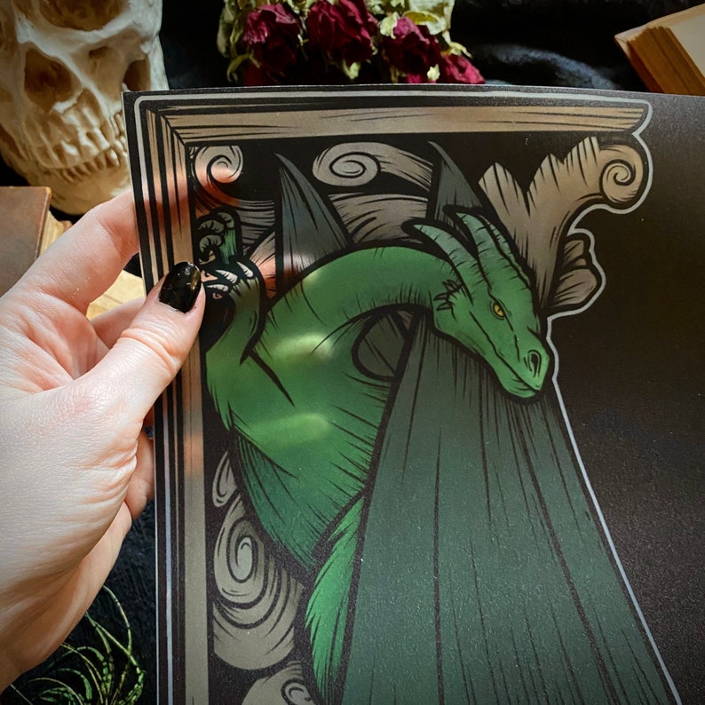 Puede incluir: Un drag&oacute;n verde con alas asoma desde detr&aacute;s de un marco decorativo. El drag&oacute;n est&aacute; dibujado en un estilo vintage con detalles intrincados.