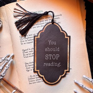 Peut inclure: Marque-page noir avec bordure dorée et le texte "You should STOP reading." Une gland noir est suspendu en haut. Le marque-page est sur un livre avec du texte français. Article décoratif.
