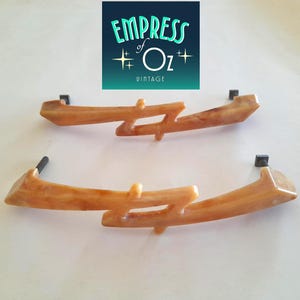 May include: Two light brown, marbled-effect drawer pulls with a jagged, asymmetrical design. Each handle features a central cutout and two dark metal mounting bolts extending from the ends. Above the pulls, a logo reads EMPRESS of Oz VINTAGE.