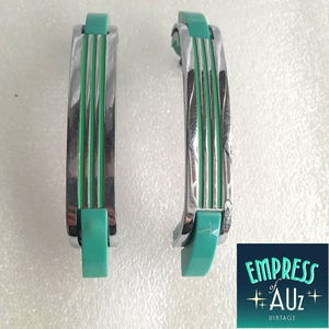 May include: Two curved drawer pulls featuring a polished chrome finish with three vertical grooves and solid mint green plastic accents at the top and bottom ends. The hardware has a sleek, elongated design with a smooth, reflective metallic surface.