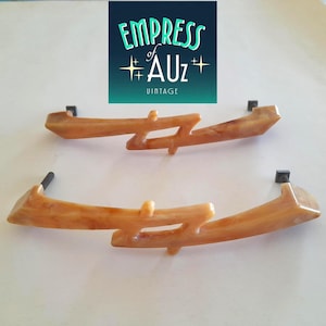 May include: Two light brown, marbled, translucent drawer pulls with a jagged, asymmetrical design. Each handle features a central cutout and two dark metal mounting posts on the ends. A logo above reads EMPRESS of AUz VINTAGE.