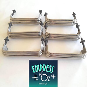 May include: A set of six silver-toned metal drawer pulls, each featuring a triple-ribbed design and two threaded mounting bolts with square nuts. A square logo graphic is positioned below the hardware, displaying the text EMPRESS of Oz VINTAGE.