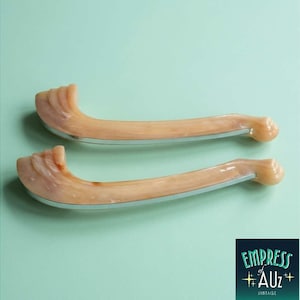May include: Two curved drawer pulls featuring a marbled peach and cream resin finish with a smooth, polished texture. Each handle has a distinct, layered design at one end and a rounded tip at the other, accented by a thin silver-toned metal base.
