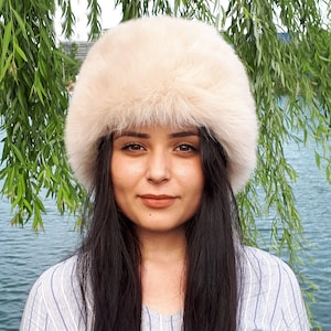 Peut inclure: Un chapeau en fausse fourrure de couleur cr&egrave;me, dot&eacute; d'une forme cylindrique et d'une texture &eacute;paisse et douce. Le chapeau pr&eacute;sente un sommet arrondi et une structure large en forme de bande qui couvre la t&ecirc;te avec un aspect dense et duveteux.